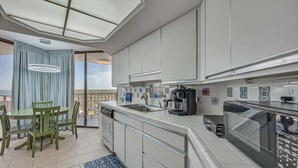 A modern kitchen with a dining area, large windows, and a view of the outdoors.