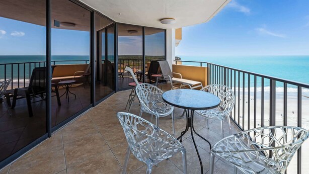 A balcony with glass doors, metal chairs, a round table, and a view of the ocean.