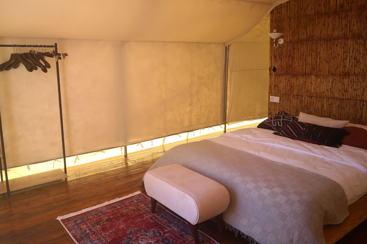 Un dormitorio con una cama grande, piso de madera, lámpara colgante y ventana con vistas.