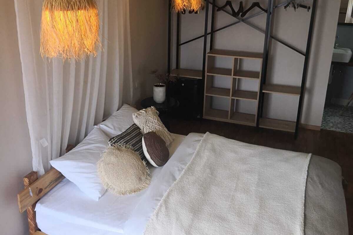 Un dormitorio con una cama, dos lámparas colgantes, cabecera de madera, una mesita de noche y un armario.
