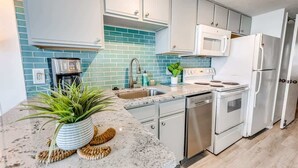 A kitchen with white cabinets, a blue backsplash, a coffee maker, a microwave, a refrigerator, and a dishwasher.