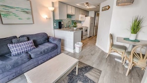 A modern apartment with a grey sofa, a small dining table, and a kitchen area with white cabinets and a microwave.