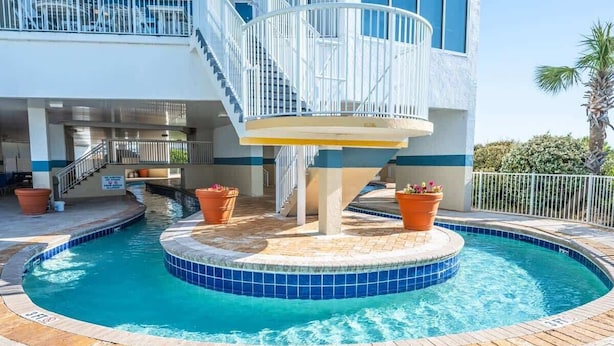 A swimming pool with a circular design, surrounded by a tiled deck and potted plants.