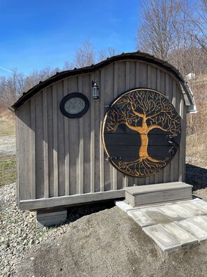 Une structure en bois dotée d’une porte circulaire ornée d’un motif d’arbre, d’une petite fenêtre et d’une lanterne.
