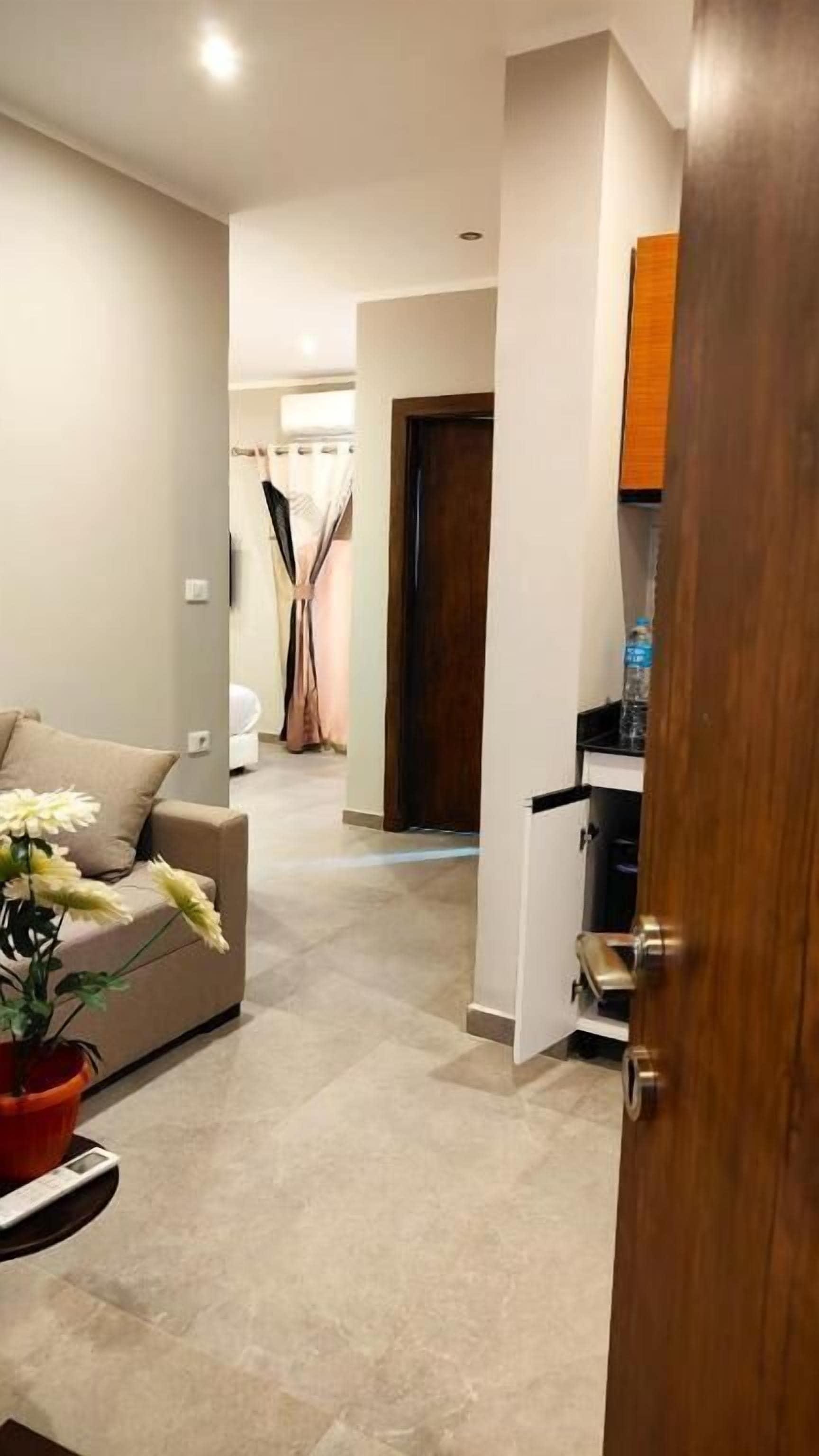 A modern living room with a beige sofa, a small table with a potted plant, and a wooden door leading to another room.