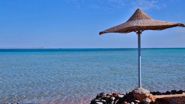 A clear blue sea with a rocky shore and a thatched umbrella structure.