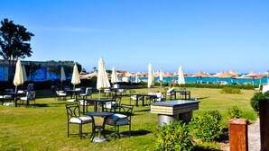 An outdoor seating area with tables and chairs, umbrellas, and a view of the beach.