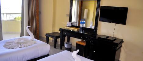 A hotel room with two beds, a desk with a mirror, a television, and a view of the outdoors.