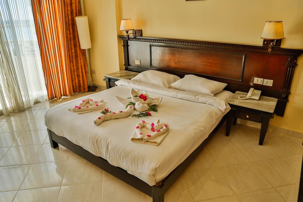 A neatly made bed with towels and flowers, a wooden headboard, bedside lamps, and a phone on a nightstand.