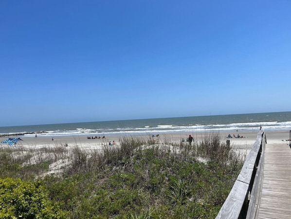 Une plage avec une promenade en bois menant au rivage, une plage de sable et des vagues de l’océan.