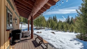 A wooden deck with outdoor seating, a grill, and a view of a snowy landscape with trees.