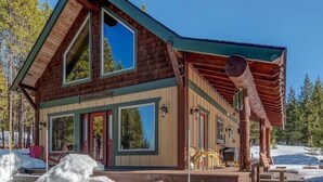 A log cabin with a steeply pitched roof, large windows, and a covered porch area.