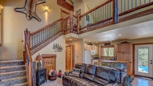 A spacious living area with a leather sofa, a staircase with wooden railings, and a kitchen in the background.