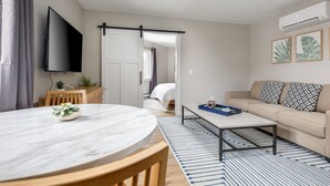 Ein modernes Wohnzimmer mit einem runden Marmortisch, einer Couch, einem Couchtisch und einem an der Wand befestigten Fernseher.