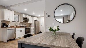 Une cuisine moderne avec des meubles blancs, un four à micro-ondes et un réfrigérateur. On y trouve une table à manger avec des chaises et un vase rempli de fleurs.