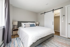 A bedroom with a bed, nightstands, a lamp, a sliding door, and a patterned rug.