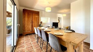 A dining area with a wooden table set for six, grey chairs, a large wooden cabinet, and a television in the background. - Teules CostaBravaSi. Swimming pool, parking, wifi (Santa Cristina d'Aro)
