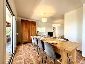 A dining area with a wooden table set for six, grey chairs, a large wooden cabinet, and a television in the background. - Teules CostaBravaSi. Swimming pool, parking, wifi (Santa Cristina d'Aro)
