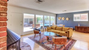 A spacious living room with a large window, a yellow sofa, a glass coffee table, and a patterned rug.