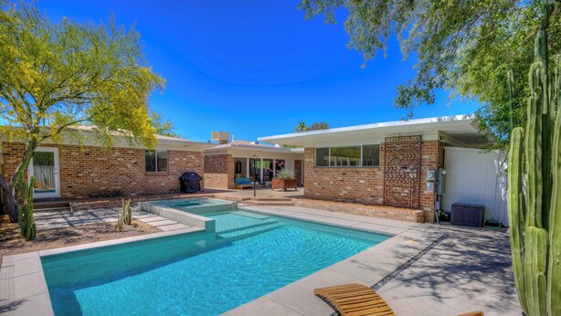 A modern house with a swimming pool, outdoor seating, and cacti.