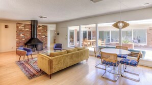 A spacious living room with a brick fireplace, a yellow sofa, and a dining area with a round table and chairs.