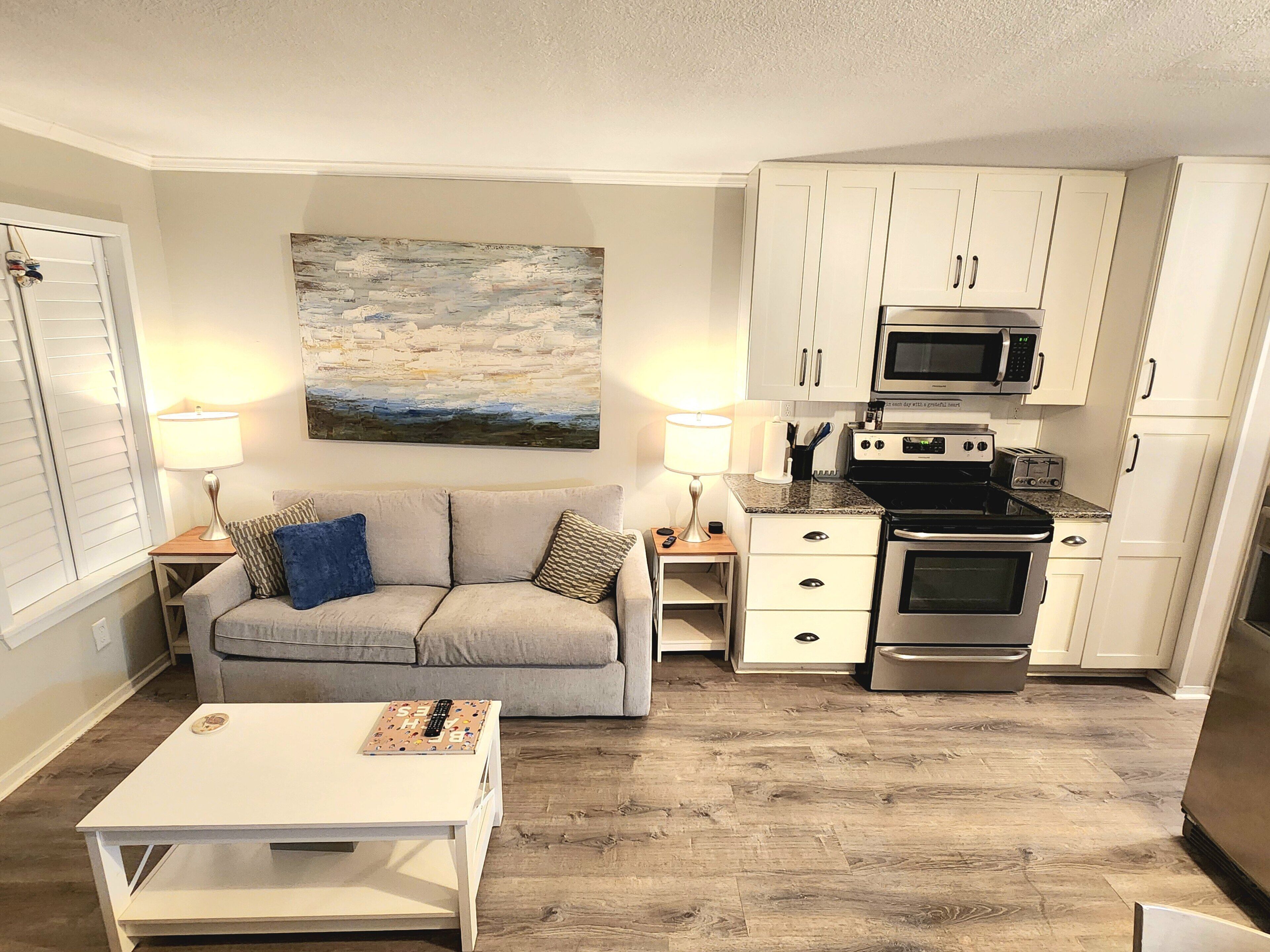A compact living space with a kitchenette, a sofa, a coffee table, and a painting on the wall.