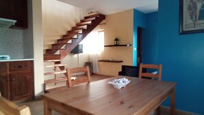 A dining area with a wooden table and chairs, a staircase, and a blue wall with a framed picture.