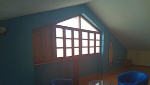 A room with a sloped ceiling, a large window with multiple panes, two blue armchairs, and a small round table.