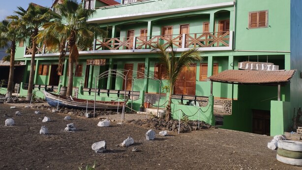 A two-story building with a green facade, wooden balconies, and a small boat docked outside.