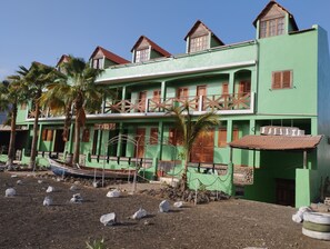 A two-story building with a green facade, wooden balconies, and a small boat docked outside. - GREEN SEA APARTMENTS (Tarrafal)