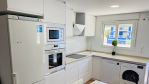 Ett modernt kök med inbyggd ugn, mikrovågsugn och diskmaskin, en diskho och ett fönster med utsikt över byggnader.