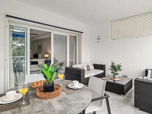 Uma sala de estar moderna com área de jantar, apresentando uma porta de vidro que dá para uma varanda, um conjunto de sofá e uma mesa de jantar com itens de café da manhã.