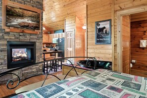 Un intérieur de chalet chaleureux avec une cheminée en pierre, des murs en bois, un coin repas et une cuisine.