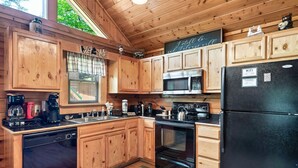 A wooden cabin kitchen with wooden cabinets, a black refrigerator, a microwave, a stove, and a sink. - Couples Cabin - Private Hot Tub - 1 Mile to Parkway (Pigeon Forge)