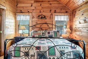 Une chambre dans un chalet en bois, avec un lit, deux fenêtres avec des rideaux et une lampe fixée au mur.