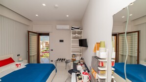 A hotel room with two beds, a desk, a chair, a TV, a balcony with a view of buildings, and a wardrobe. - Casa Christal (Sant´Agnello)