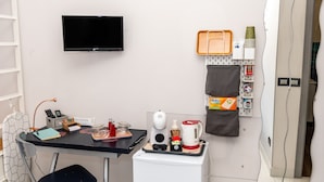A compact hotel room with a flat-screen TV mounted on the wall, a small kitchenette with a coffee maker, tea, and condiments, and a desk with a lamp and a phone. - Casa Christal (Sant´Agnello)