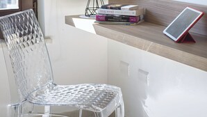 A clear plastic chair, a small table with a lamp, and a few books on a shelf. - Casa Cristina Green (Sorrento)