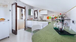 A compact kitchen with white cabinets, a green countertop, and a dining area with a white chair. - Casa Cristina Green (Sorrento)