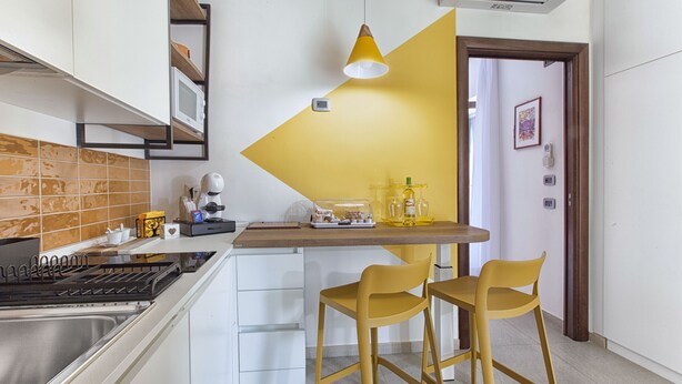 A kitchen with a microwave, stove, and yellow chairs. - Casa Cristina: yellow apartment (Sorrento)