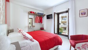 A bedroom with a bed, a red chair, a TV, and a balcony with a view. - Casa Cristina: yellow apartment (Sorrento)