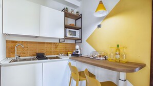 A modern kitchen with white cabinets, a microwave, a sink, and a wooden countertop with bar stools. - Casa Cristina: yellow apartment (Sorrento)