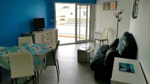Una habitación con una mesa de comedor, sillas, un sofá, un televisor y un ventanal corredero que da a un espacio exterior.