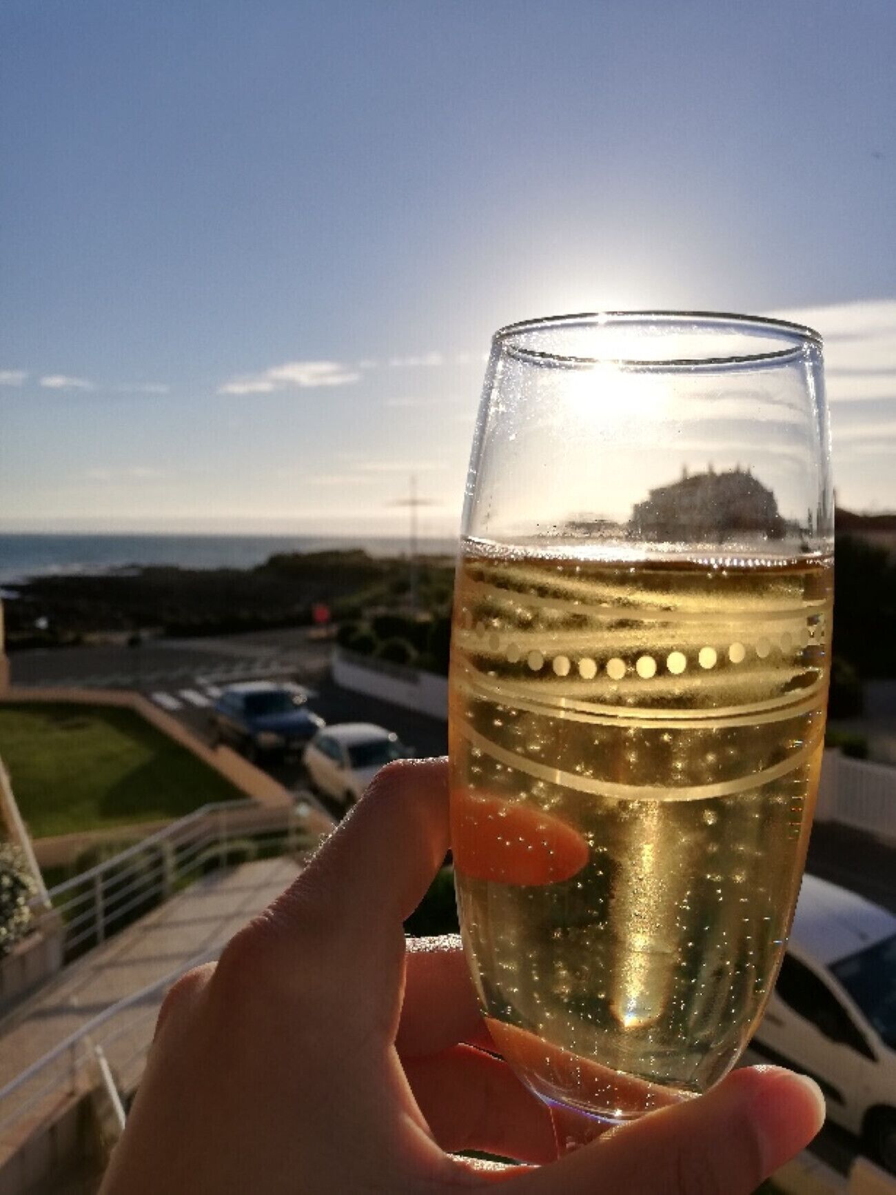 Eine Hand hält ein Glas Weißwein, im Hintergrund eine Küstenlandschaft.