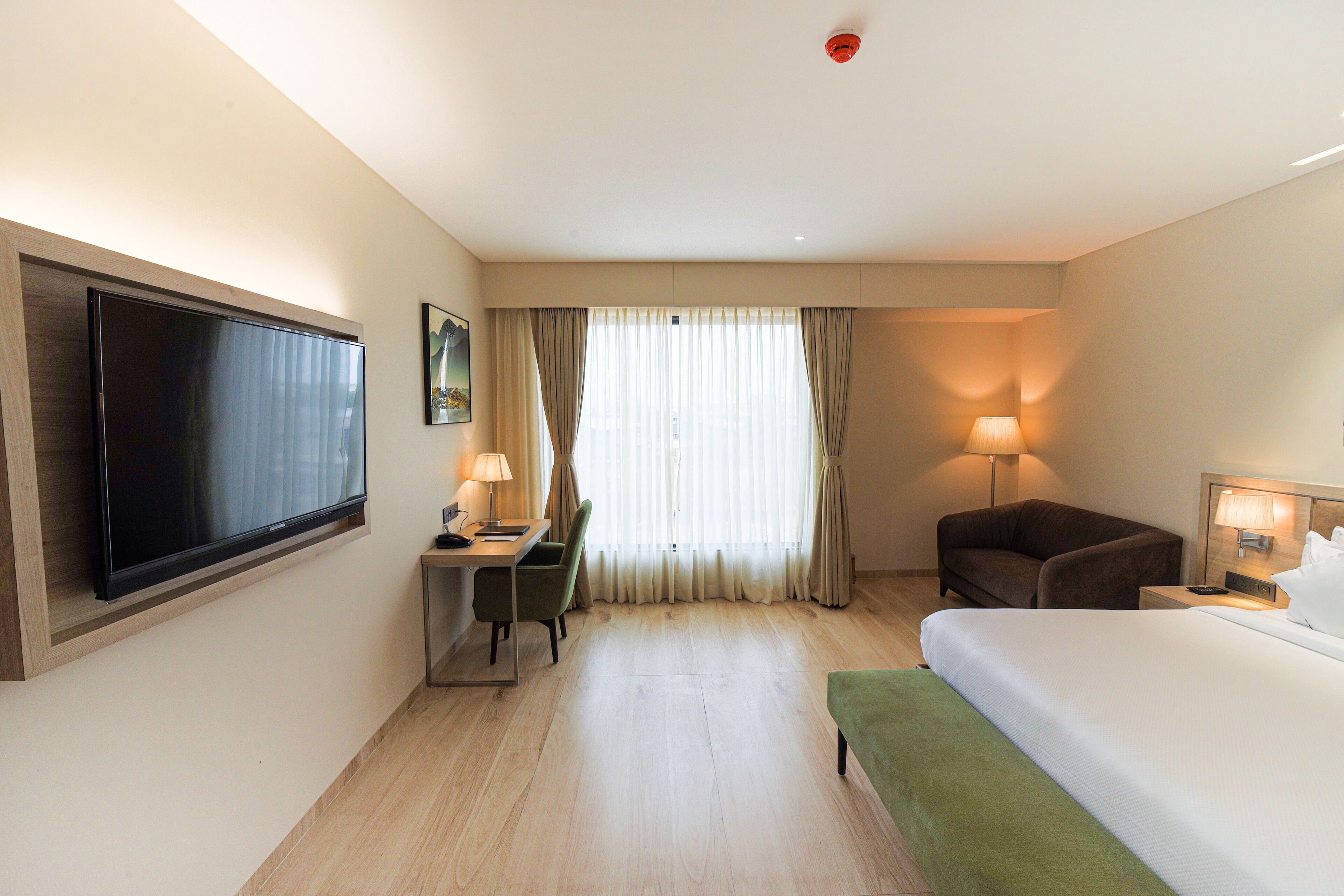 A hotel room with a bed, a desk with a chair, a television, and a lamp.