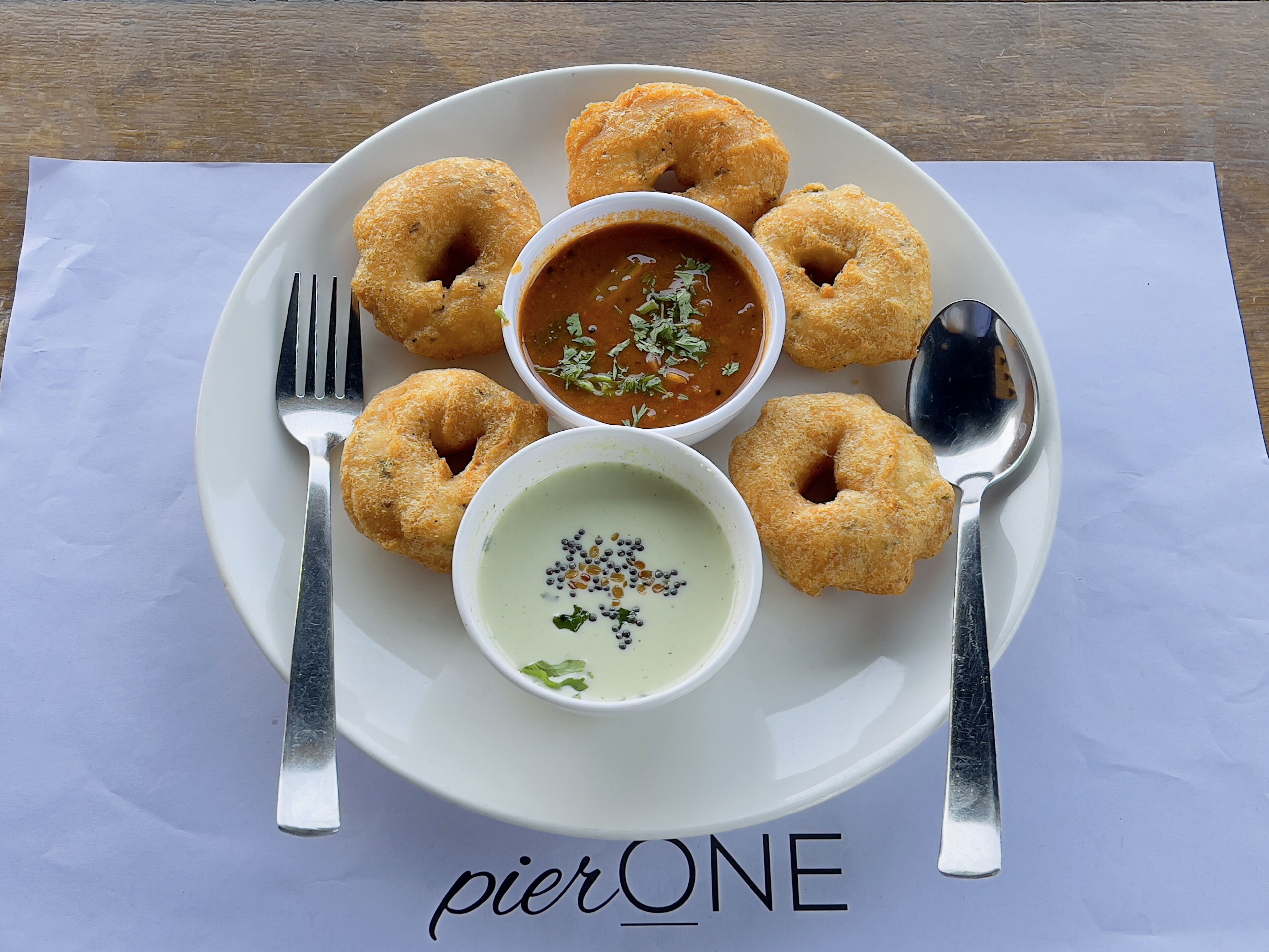 Un plato con seis rosquillas fritas y dos recipientes con salsas para mojar sobre un mantel blanco.