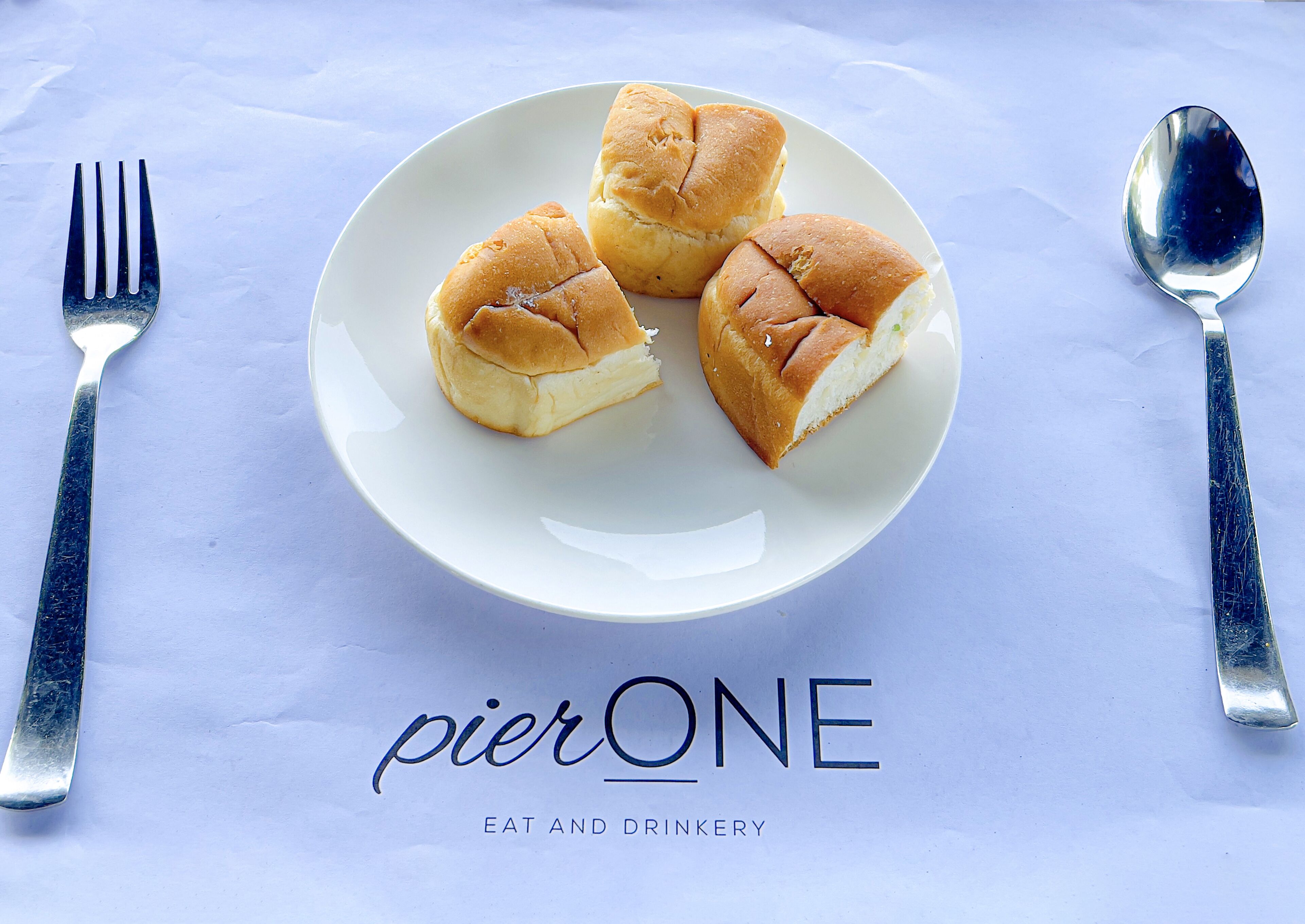 A plate with three rolls of bread on a white tablecloth with the text "pierONE EAT AND DRINKERY" below.