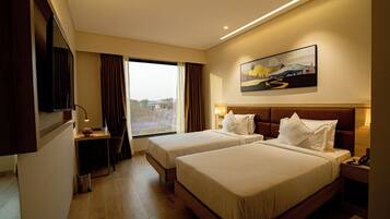 A hotel room with two beds, a desk, a TV, and a window with curtains.
