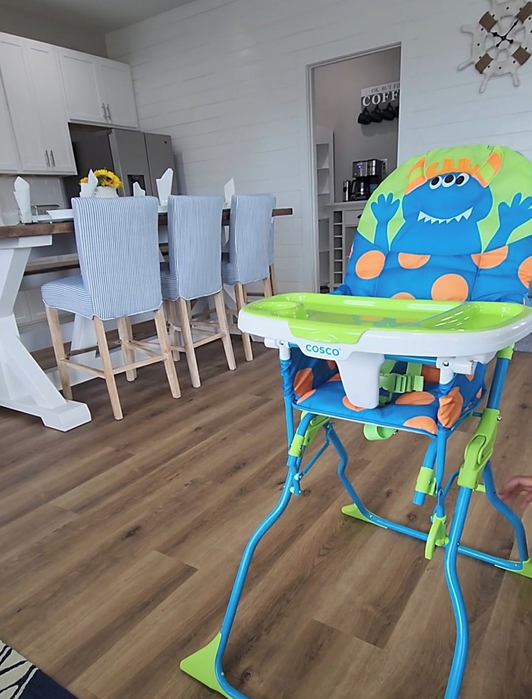 A modern kitchen with white cabinets, a dining area with striped chairs, and a colorful children's high chair.