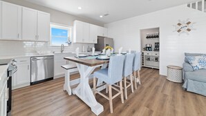 A modern kitchen with white cabinets, a wooden dining table, and striped chairs. - Private beach/Luxury home/Private pool (Gulf Shores)